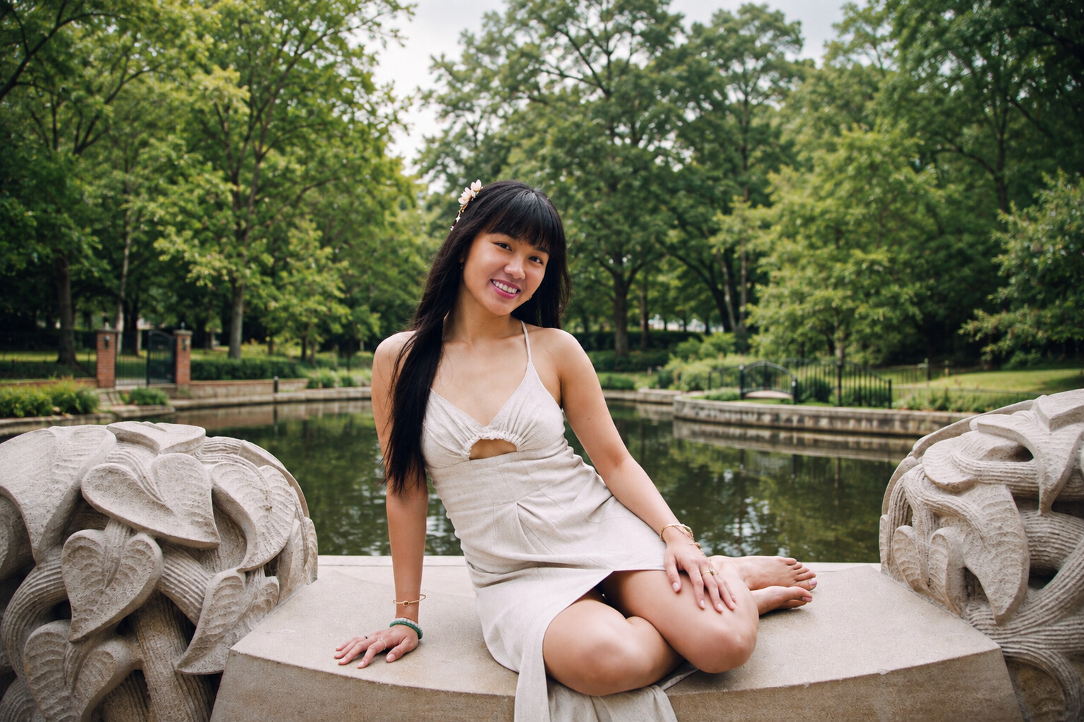 Grace smiling, seated between two stone sculptures by the water